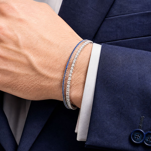 Due bracciali tennis in oro bianco con zaffiri blu e diamanti, indossati al polso di un uomo in abito blu.